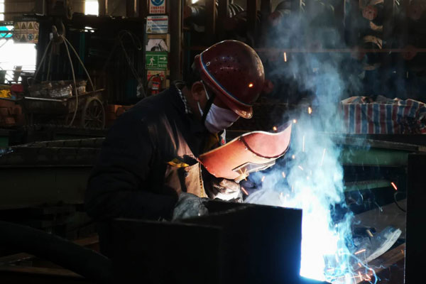 一名工人戴著口罩對設備進行焊接。