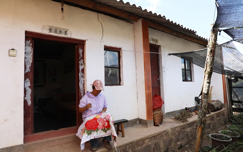 2017年之前字雲輝一家4口住的石綿瓦房。圖為妻子李海妹正在房前縫十字繡。（楊佳燕 攝）