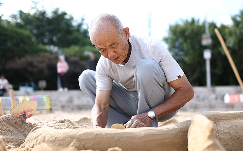 在聂耳广场沙滩上，“沙雕爷爷”正专心致志地做着大象沙雕。刘芳摄