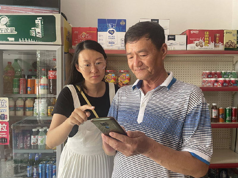 工作人员（左）指导零售户使用网上办证小程序。罗丹摄