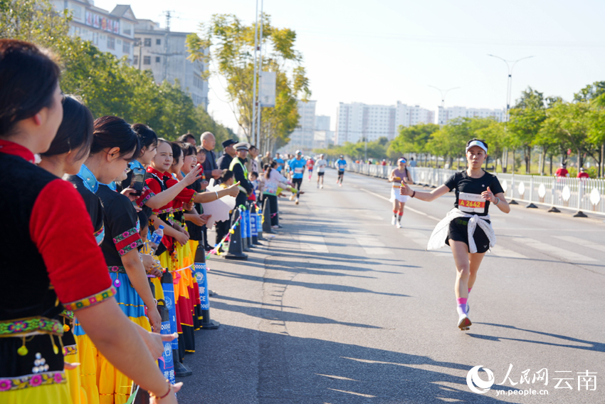 2026普洱思茅馬拉鬆跑者少數民族啦啦拉隊員互動。人民網 王嫻攝