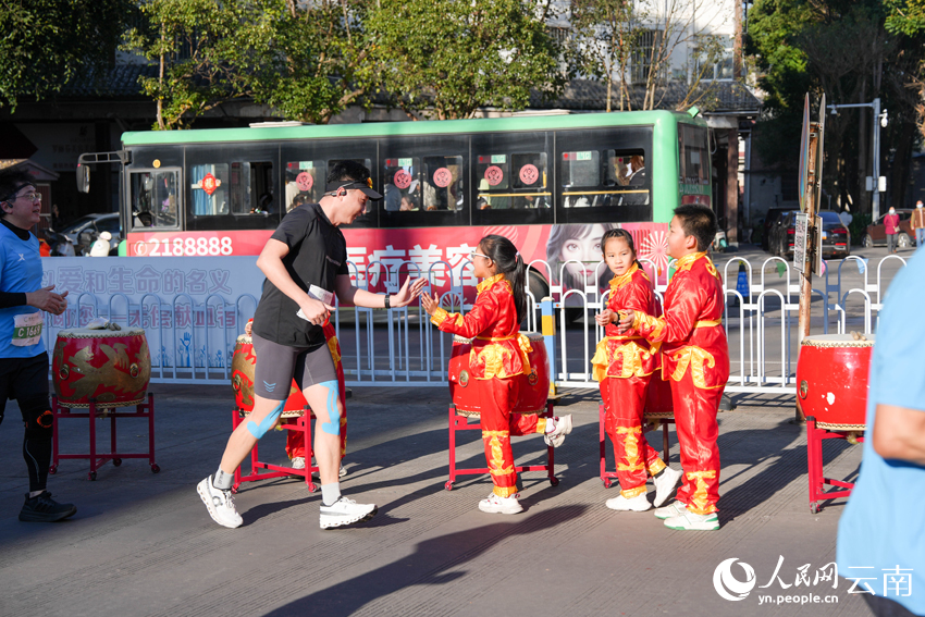 2026普洱思茅馬拉鬆跑者與沿途啦啦隊小朋友互動。人民網 王嫻攝