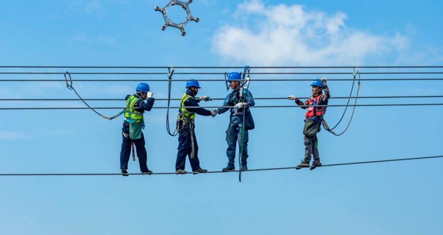 2月5日，中老500千伏联网工程全线贯通后，国内段与老挝段工作人员在跨境段导线安装间隔棒过程中握手祝贺。云南电网公司供图