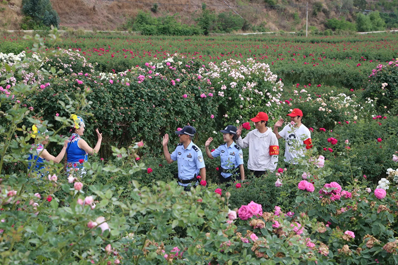 光禄派出所民警和辖区治安员在东方玫瑰谷景区和身着民族服装的游客挥手互动。