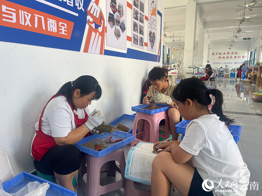 【3】刘云琼埋头加工首饰配件,儿子来到车间体验母亲日常的劳作,女儿坐在一旁,低头书写暑假作业。人民网记者-程浩摄